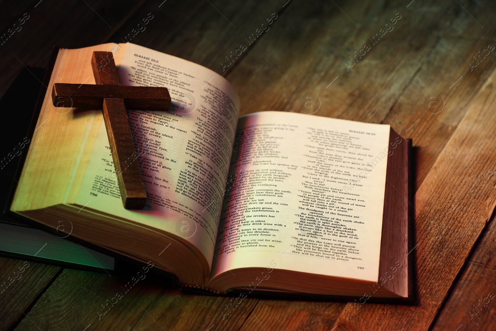 Photo of Cross and Bible on wooden table in color lights, closeup. Religion of Christianity