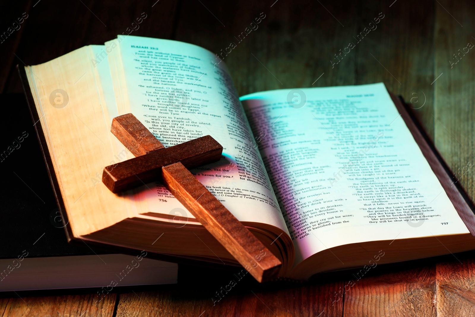 Photo of Cross and Bible on wooden table in color lights, closeup. Religion of Christianity