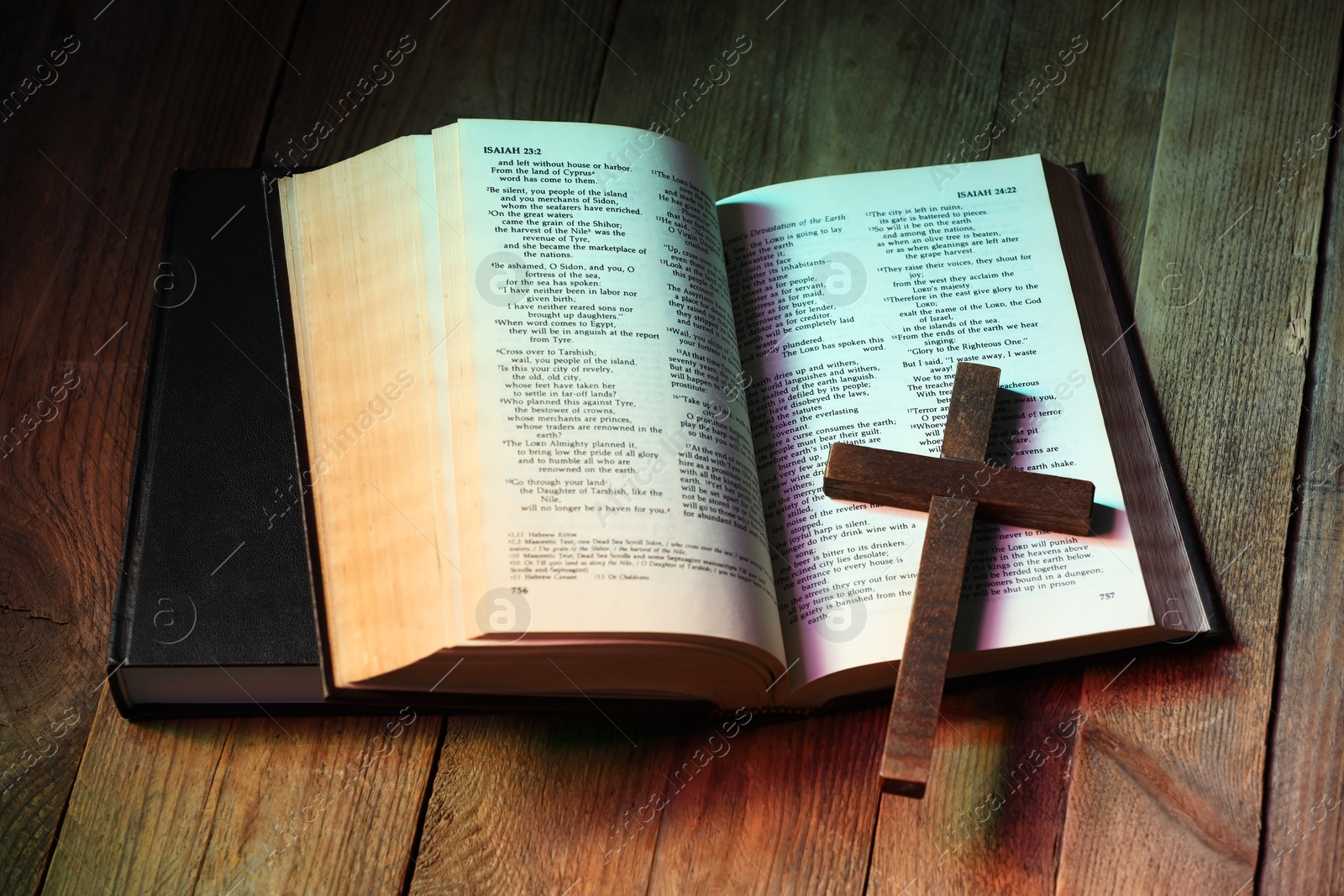 Photo of Cross and Bible on wooden table in color lights, above view. Religion of Christianity