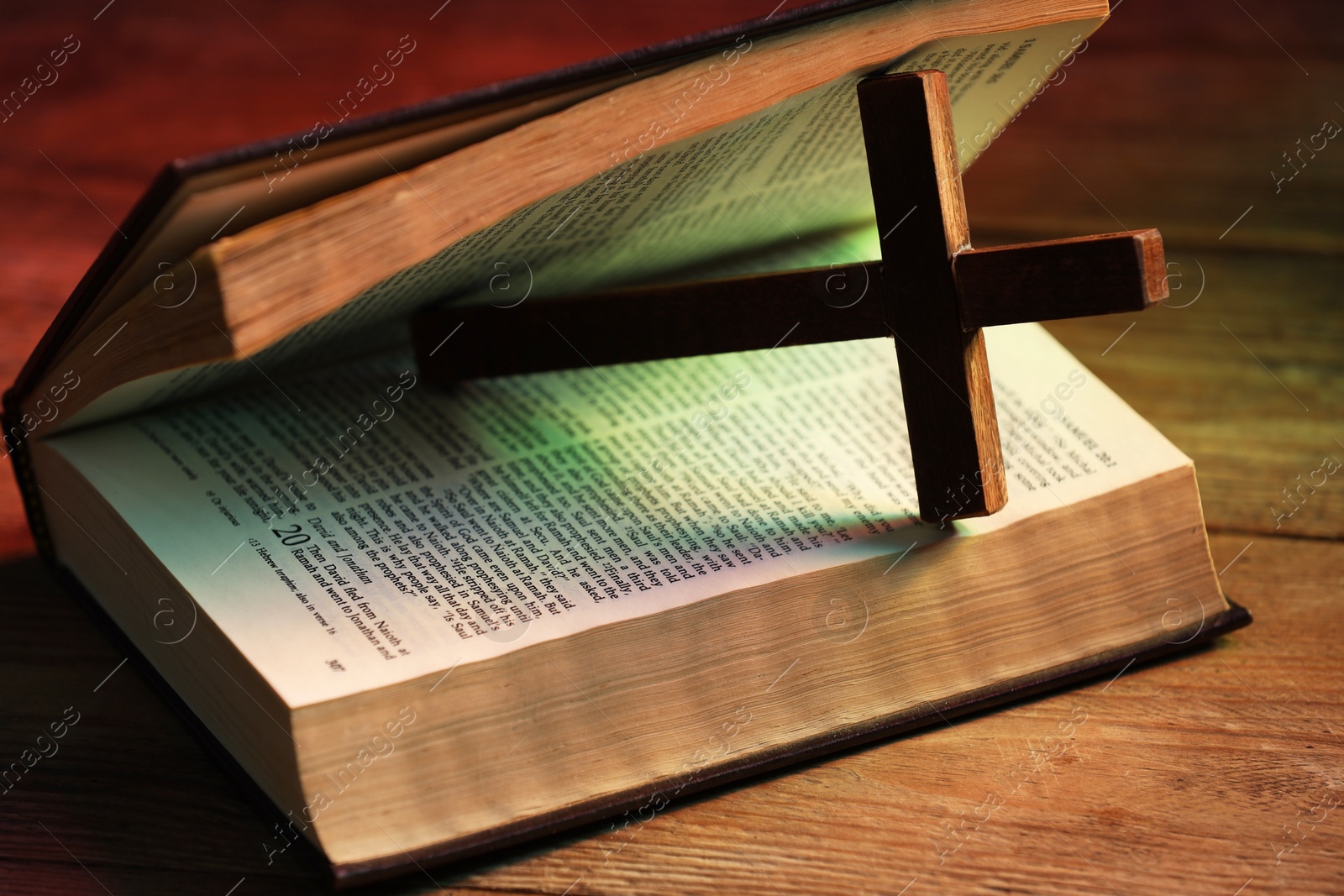 Photo of Cross and Bible on wooden table in color lights, closeup. Religion of Christianity