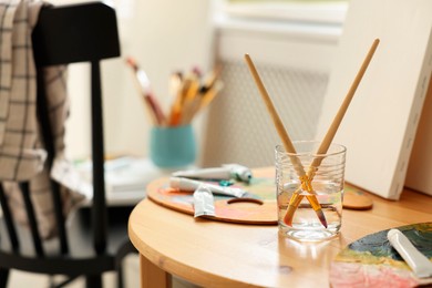 Artist's palette, brushes in glass of water and paints on wooden table indoors. Space for text