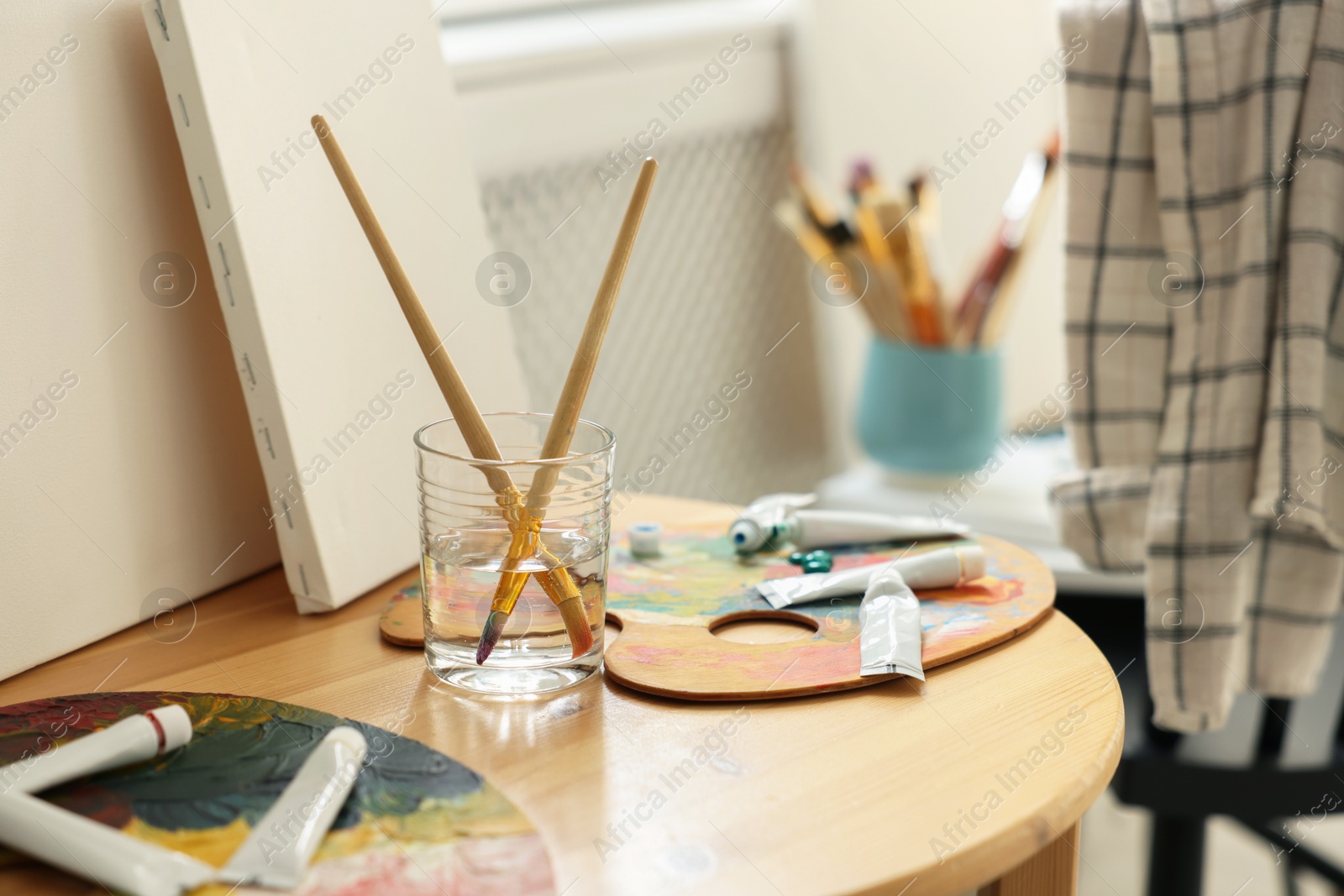 Photo of Artist's palette, brushes in glass of water and paints on wooden table indoors