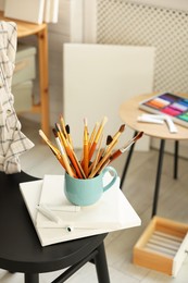 Canvases, paints and cup of brushes on chair in workshop