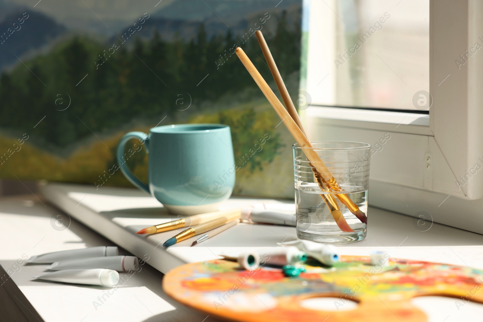 Photo of Artist's palette, brushes in glass of water and paints on window sill