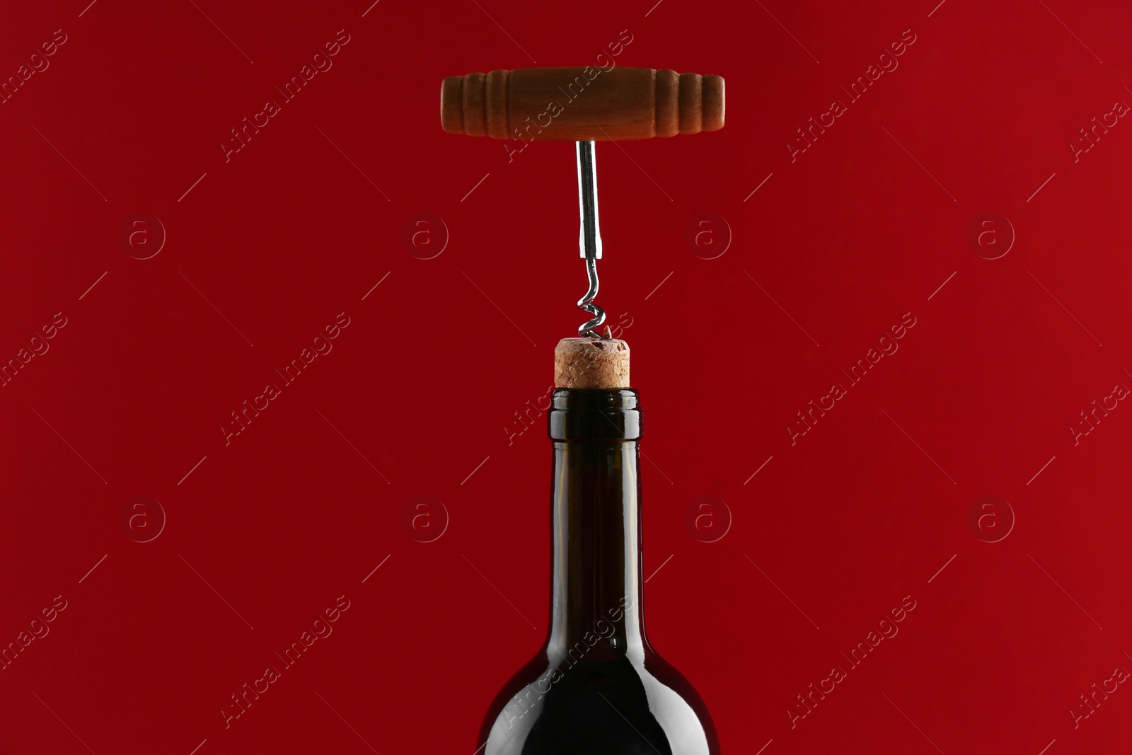 Photo of Bottle with corkscrew on red background, closeup