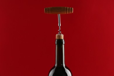 Photo of Bottle with corkscrew on red background, closeup