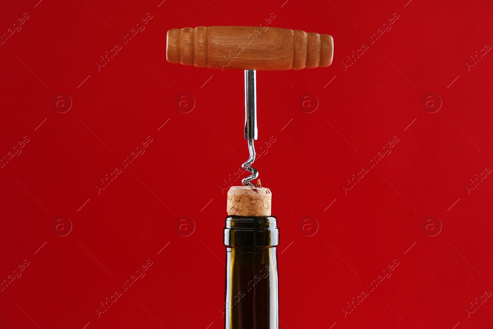 Photo of Bottle with corkscrew on red background, closeup