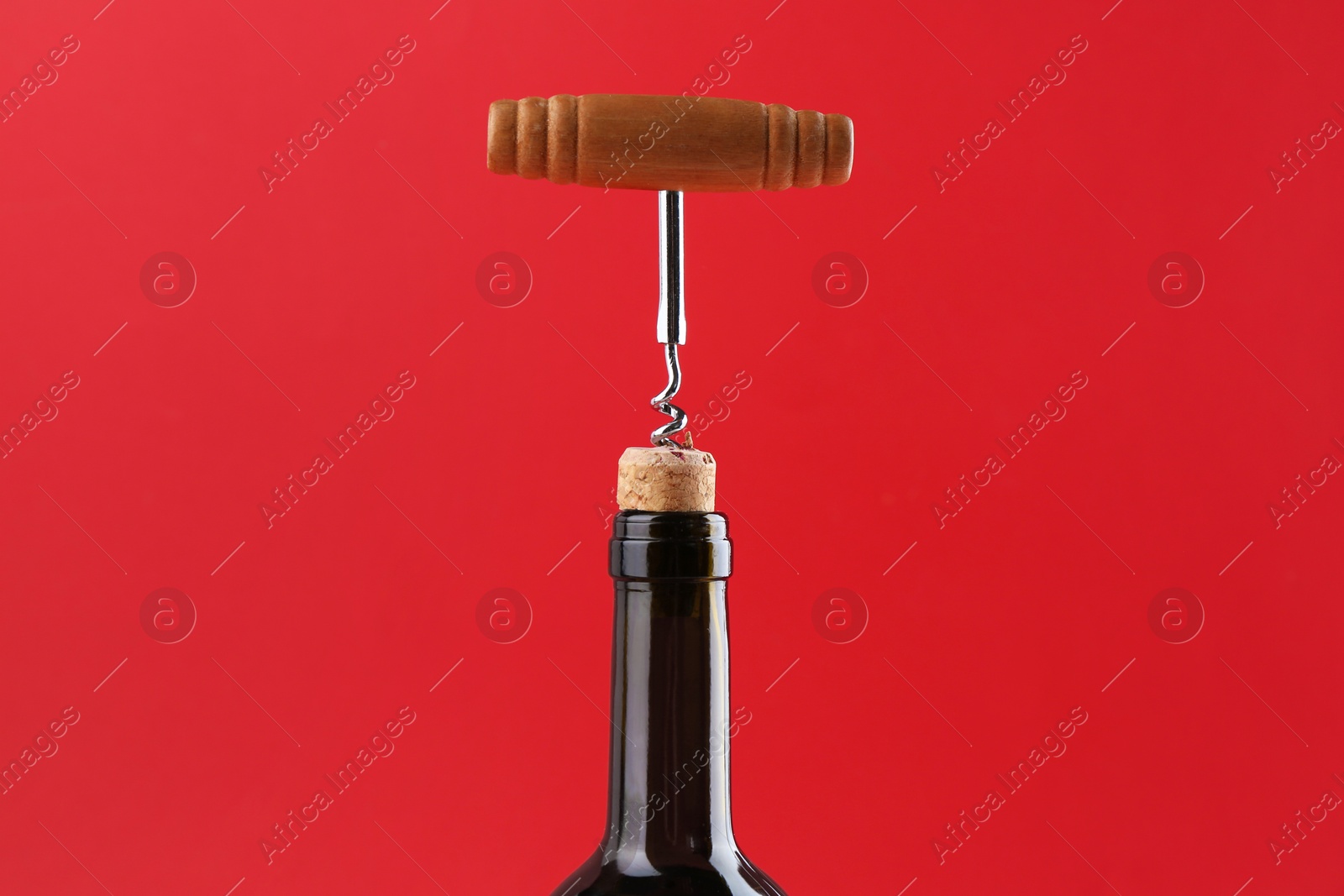 Photo of Bottle with corkscrew on red background, closeup