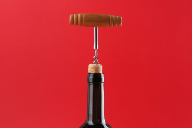 Photo of Bottle with corkscrew on red background, closeup