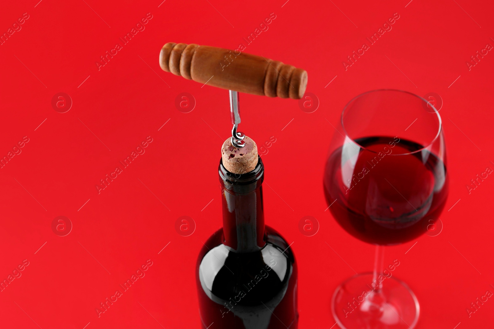 Photo of Bottle with corkscrew and glass of wine on red background, closeup