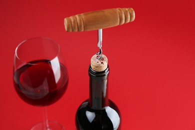 Photo of Bottle with corkscrew and glass of wine on red background, closeup