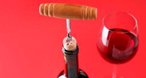 Photo of Bottle with corkscrew and glass of wine on red background, closeup. Space for text