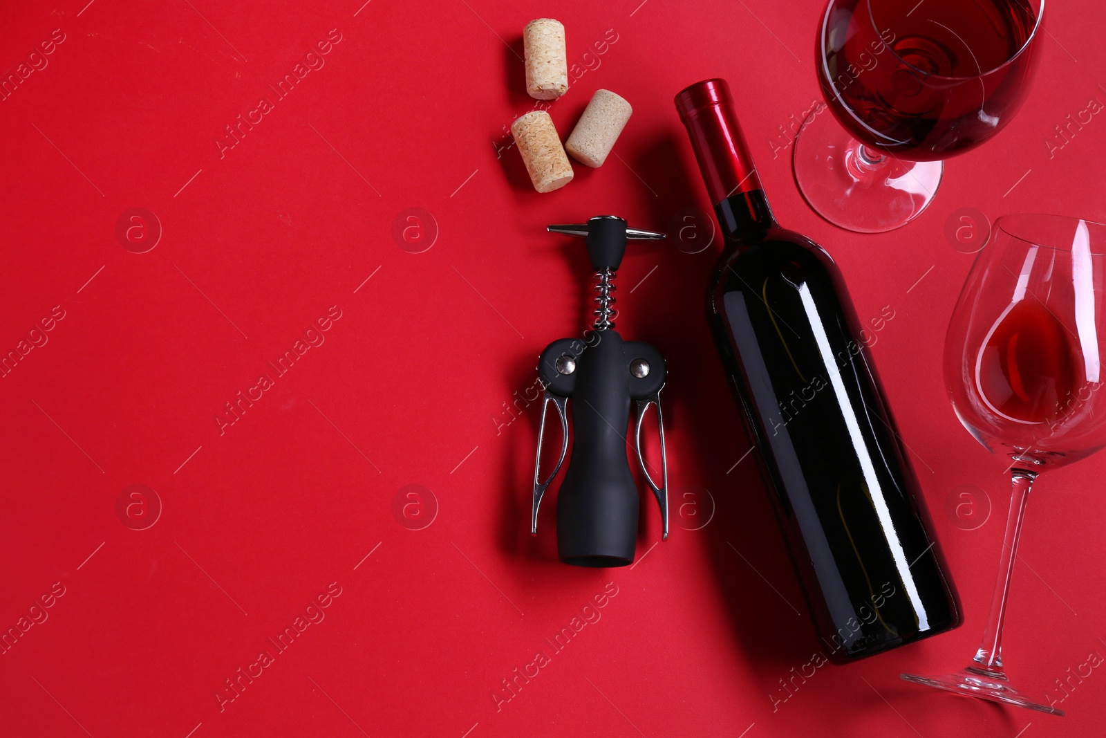 Photo of Wing corkscrew, wine and corks on red background, flat lay. Space for text