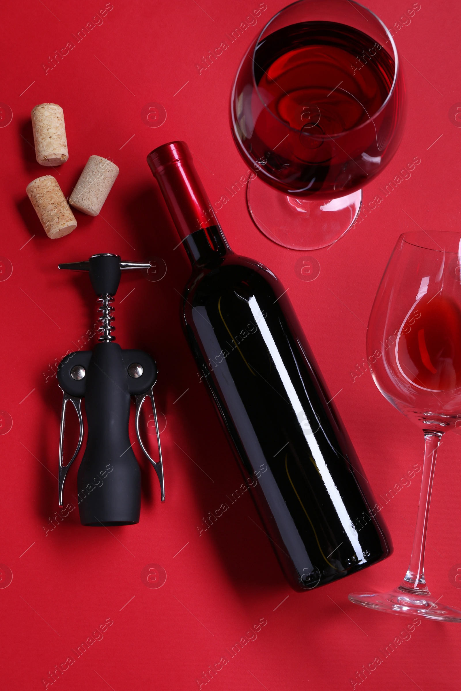 Photo of Wing corkscrew, wine, glasses and corks on red background, flat lay