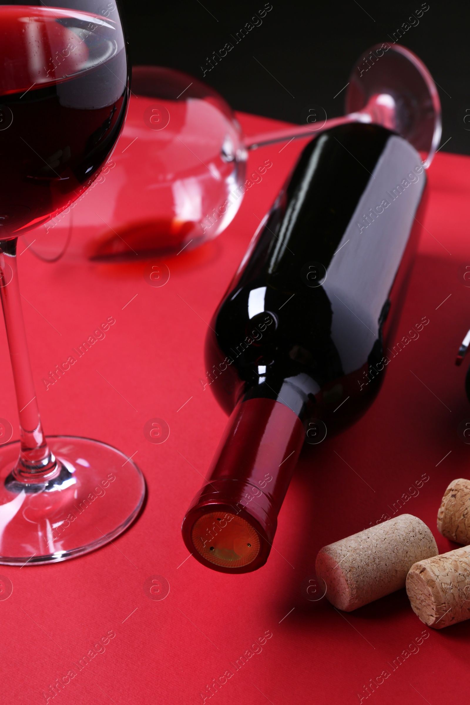 Photo of Bottle of wine, glasses and corks on red table, closeup