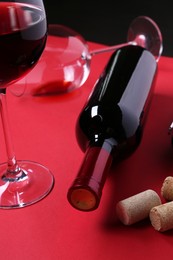 Photo of Bottle of wine, glasses and corks on red table, closeup