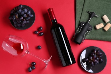 Flat lay composition with wing corkscrew and bottle of wine on red background