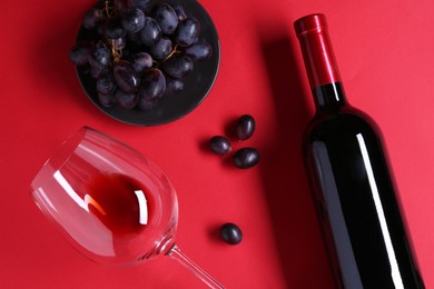 Bottle wine, glass and grapes on red background, flat lay