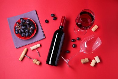 Flat lay composition with wooden corkscrews and bottle of wine on red background