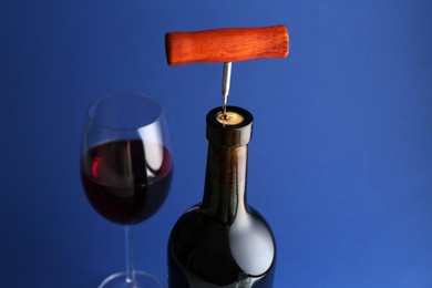 Photo of Bottle with corkscrew and glass of wine on blue background, closeup