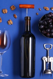 Flat lay composition of bottle with corkscrew and grapes on blue background