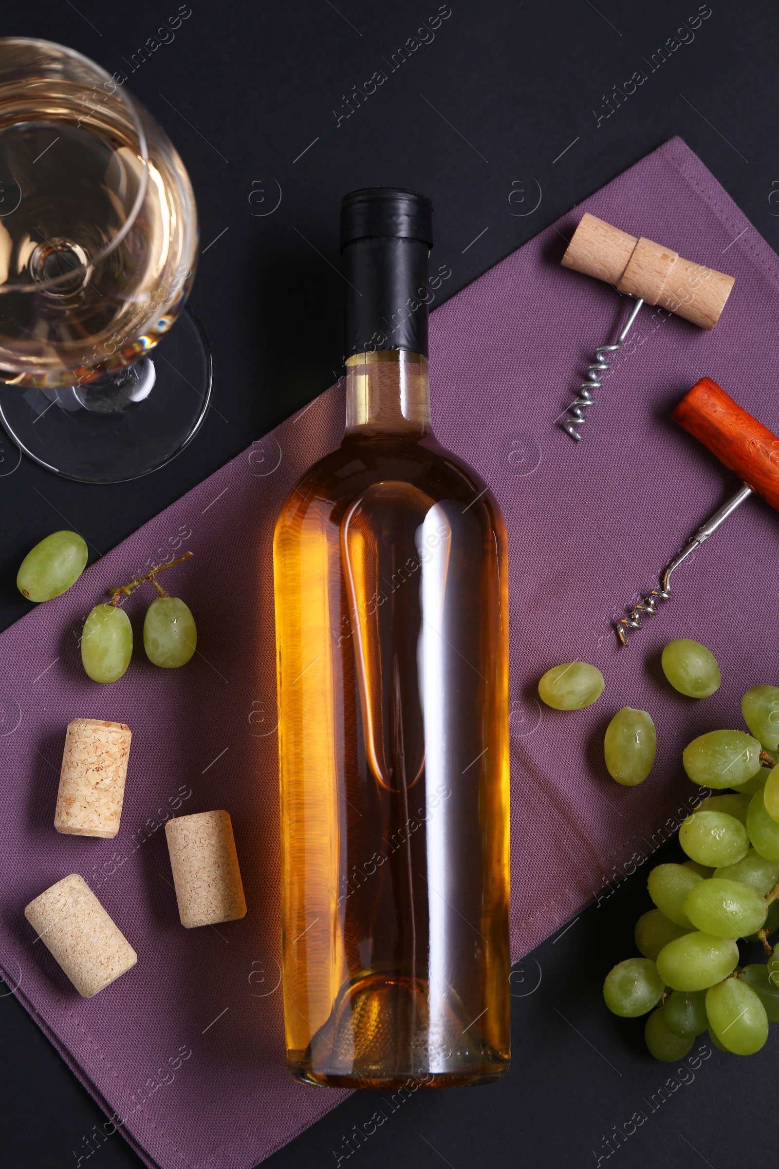 Photo of Corkscrews, wine, grapes and corks on black background, flat lay