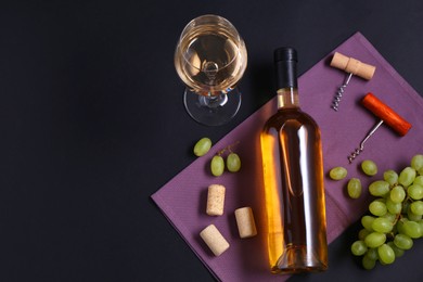 Corkscrews, wine, grapes and corks on black background, flat lay. Space for text