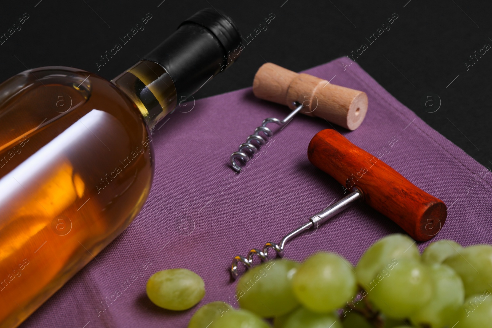 Photo of Corkscrews, wine and grapes on black background, closeup