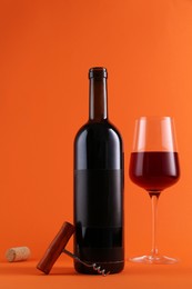 Corkscrew, glass and bottle of red wine on orange background