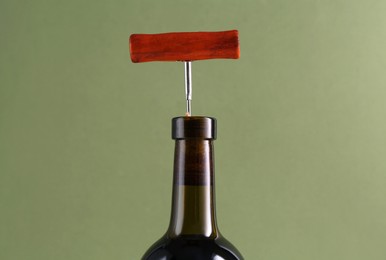 Photo of Wine bottle with corkscrew on olive background, closeup