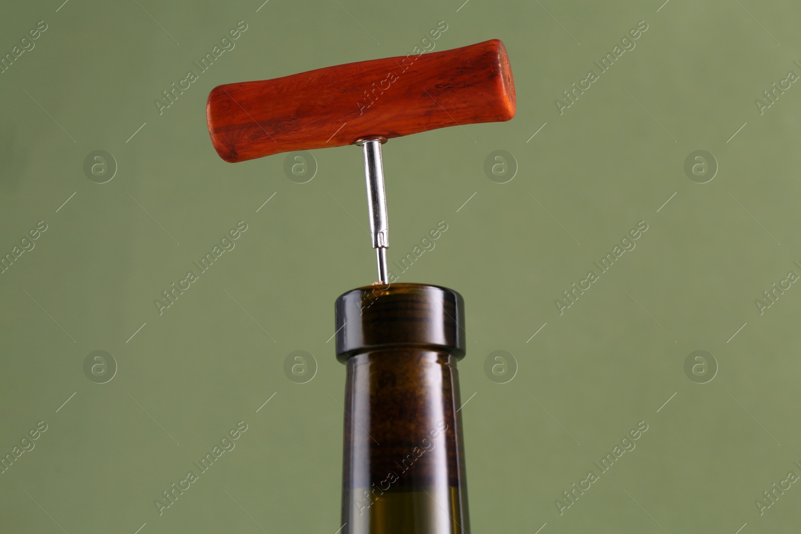 Photo of Wine bottle with corkscrew on olive background, closeup