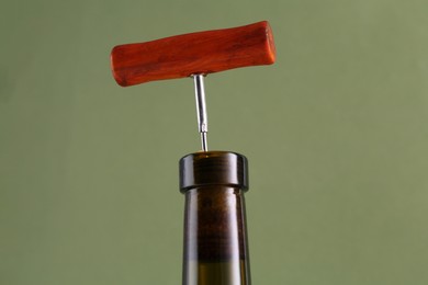 Wine bottle with corkscrew on olive background, closeup