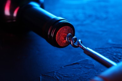 Photo of Wine bottle with corkscrew in lights on table, closeup