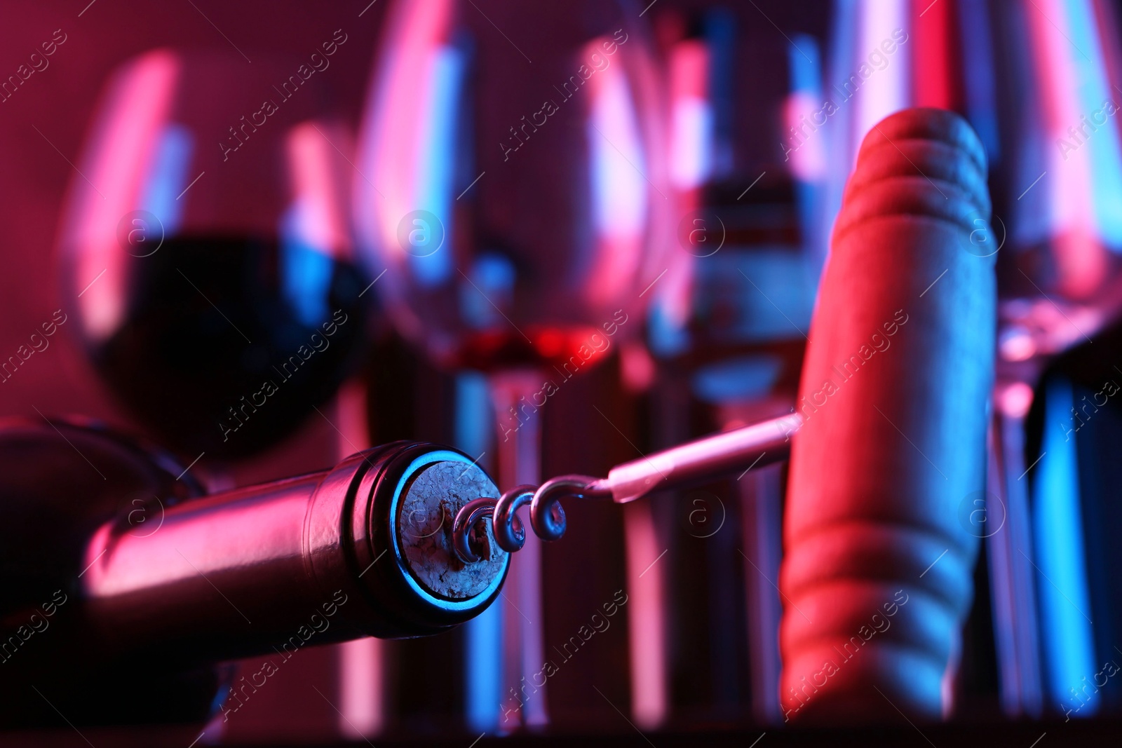 Photo of Wine bottle with corkscrew in lights on blurred background, closeup