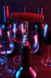 Wine bottle with corkscrew in lights on blurred background, closeup