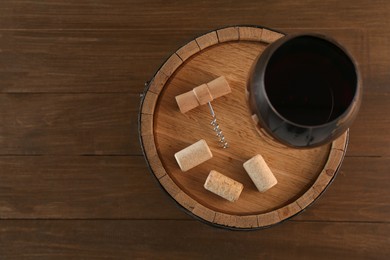 Photo of Corkscrew, corks, glass of wine and barrel on wooden, top view. Space for text