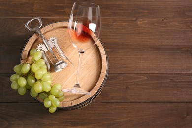 Photo of Wing corkscrew, glass, grapes and barrel on wooden table, top view. Space for text