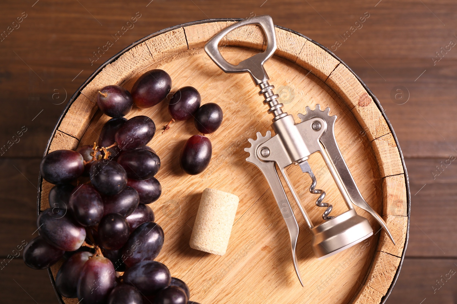 Photo of Wing corkscrew, cork, grapes and barrel on wooden table, top view