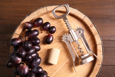 Photo of Wing corkscrew, cork, grapes and barrel on wooden table, top view