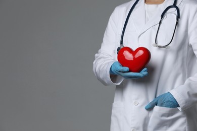 Photo of Doctor with red heart on grey background, closeup. Space for text