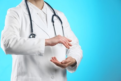 Doctor holding something on light blue background, closeup. Space for text