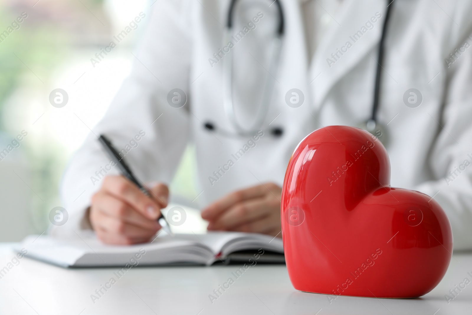 Photo of Doctor working at table in clinic, focus on red heart