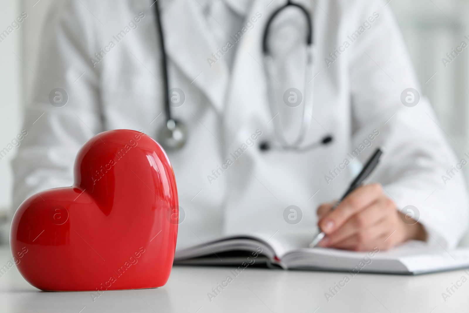 Photo of Doctor working at table in clinic, focus on red heart