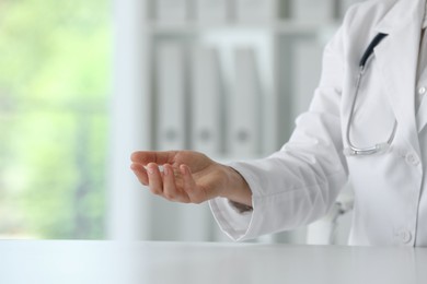 Photo of Doctor with stethoscope holding something at table in clinic, closeup. Space for text