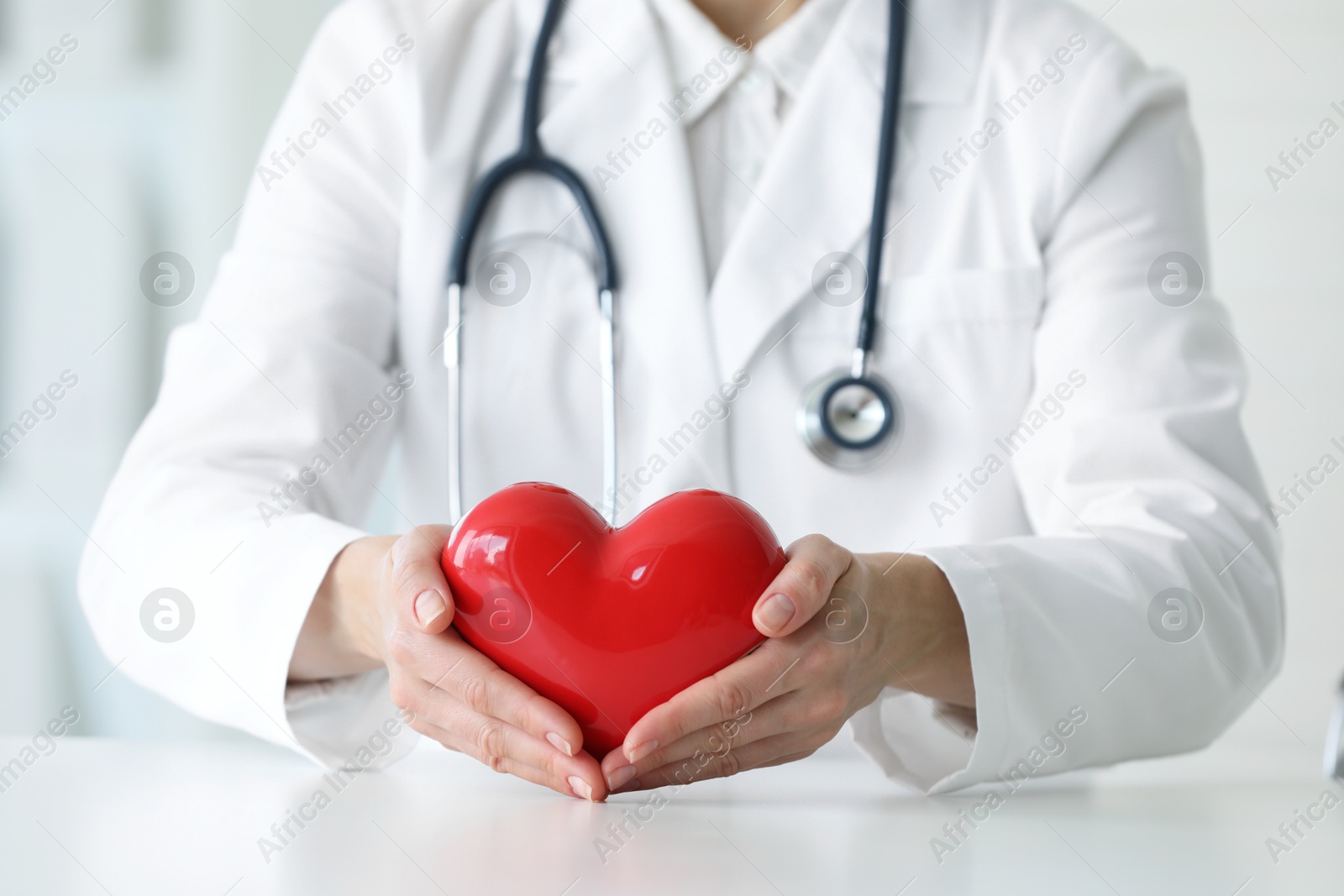 Photo of Doctor with red heart at table in clinic, closeup