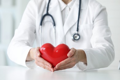 Photo of Doctor with red heart at table in clinic, closeup