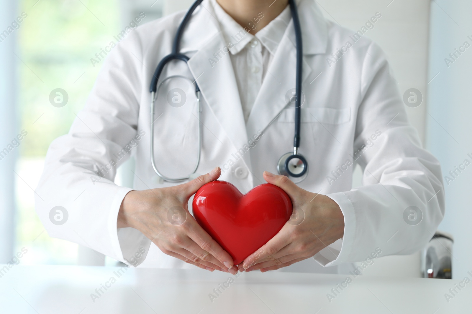 Photo of Doctor with red heart at table in clinic, closeup