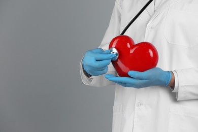 Photo of Doctor with stethoscope and red heart on grey background, closeup. Space for text