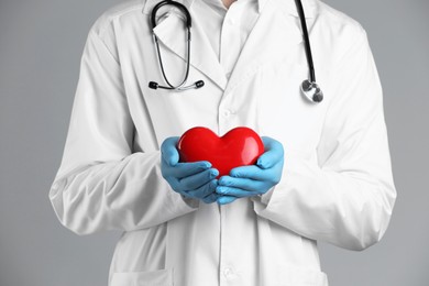 Doctor with red heart on grey background, closeup