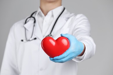 Doctor with red heart on grey background, selective focus